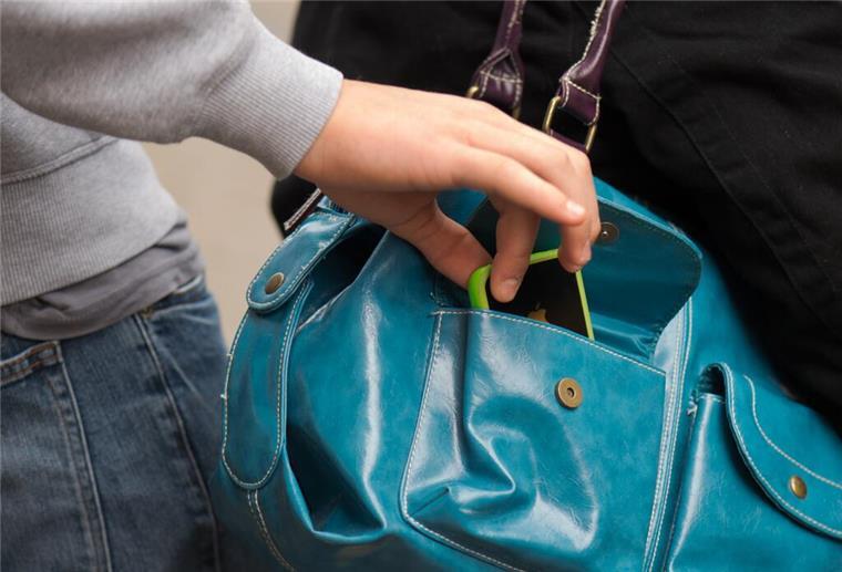 Ein Taschendieb klaut ein Handy aus einer Handtasche.