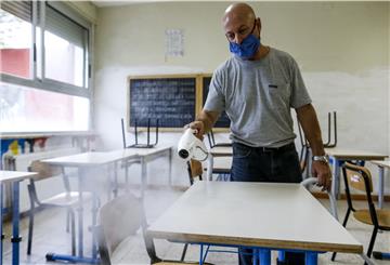Ein Mann mit Mundschutz desinfiziert Schreibtische in einem Klassenzimmer.
