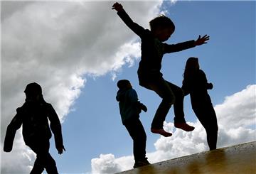 Kinder springen auf einer Hüpfburg und heben sich dabei als Schatten vom Himmel ab. 