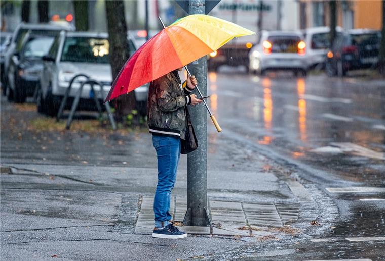 Warnmeldung: Gewitter und Starkregen in Bremerhaven möglich Ein Mann steht während einem Regenschauer mit einem bunten Regenschirm an einer Kreuzung. Für diesen Mittwoch werden im Freistaat Regen- und Gewitterschauer erwartet.