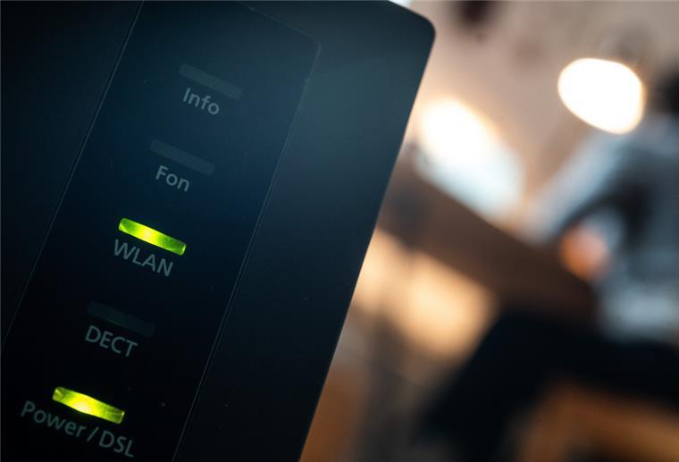 Umfrage: Mehr als jeder Dritte beklagt Internetprobleme Ein Router, auf dem die LED für W-Lan und DSL leuchten, ist in einer Wohung zu sehen, in der eine Person an einem Tisch sitzt.