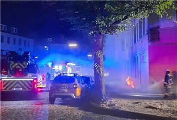 Polizei und Feuerwehrwagen stehen nachts auf einer verrauchten Straße.