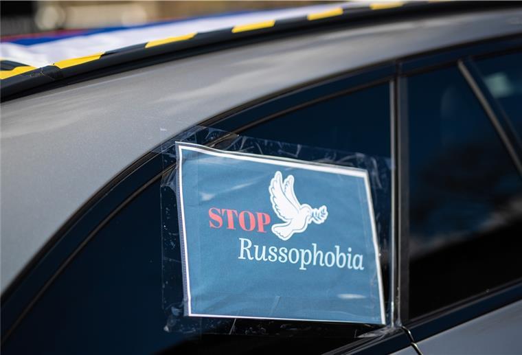 «"Stop Russophobia"» steht auf Plakaten geschrieben, das bei einem Autokorso an einem Auto angebracht ist. 