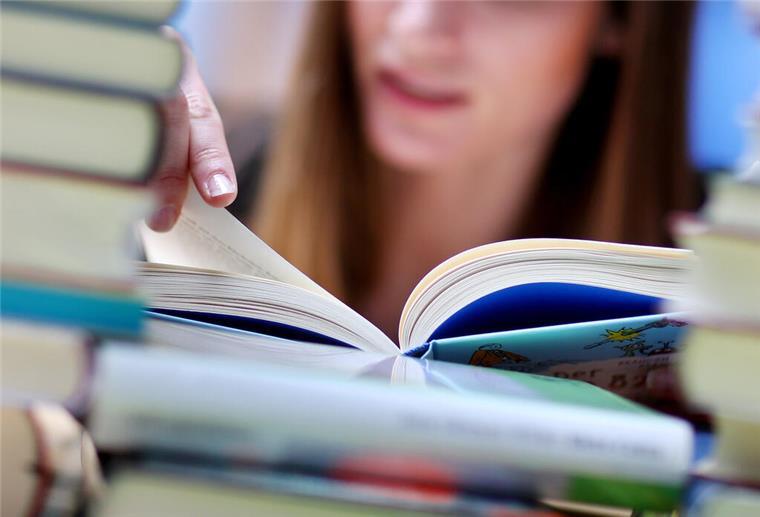 Diskriminierende Inhalte in Bremer Schulbüchern: Verlage reagieren Eine junge Frau liest an einem Tisch voller Bücher.