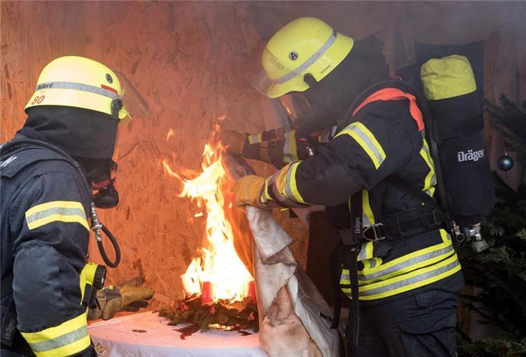 Feuerwehrleute löschen während einer Vorführung einen brennenden Adventskranz mit Hilfe einer Löschdecke.