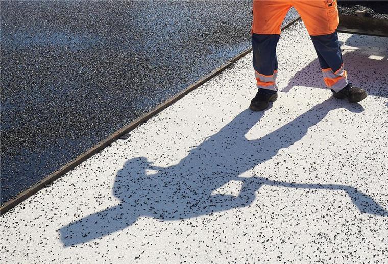 Umleitung und Behinderungen wegen Sanierung im Kreis Rotenburg Der Schatten eines Bauarbeiters fällt auf den Boden einer Straße, die asphaltiert wird.