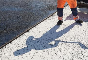 Der Schatten eines Bauarbeiters fällt auf den Boden einer Straße, die asphaltiert wird. 