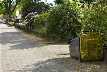 Eine Gelbe Tonne liegt neben dem Fußweg