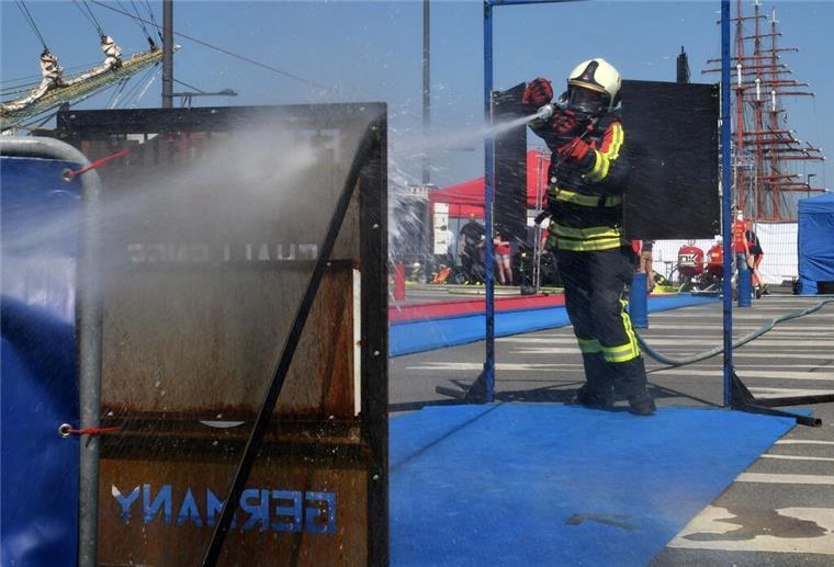 Firefighter Combat Challenge sorgt in Bremerhaven für Action Ein Feuerwehrmann in Schutzausrüstung spritzt während eines Wettbewerbs mit seinem Löschschlauch auf ein Ziel.