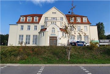 Villa, im Vordergrund ein Parkplatz.