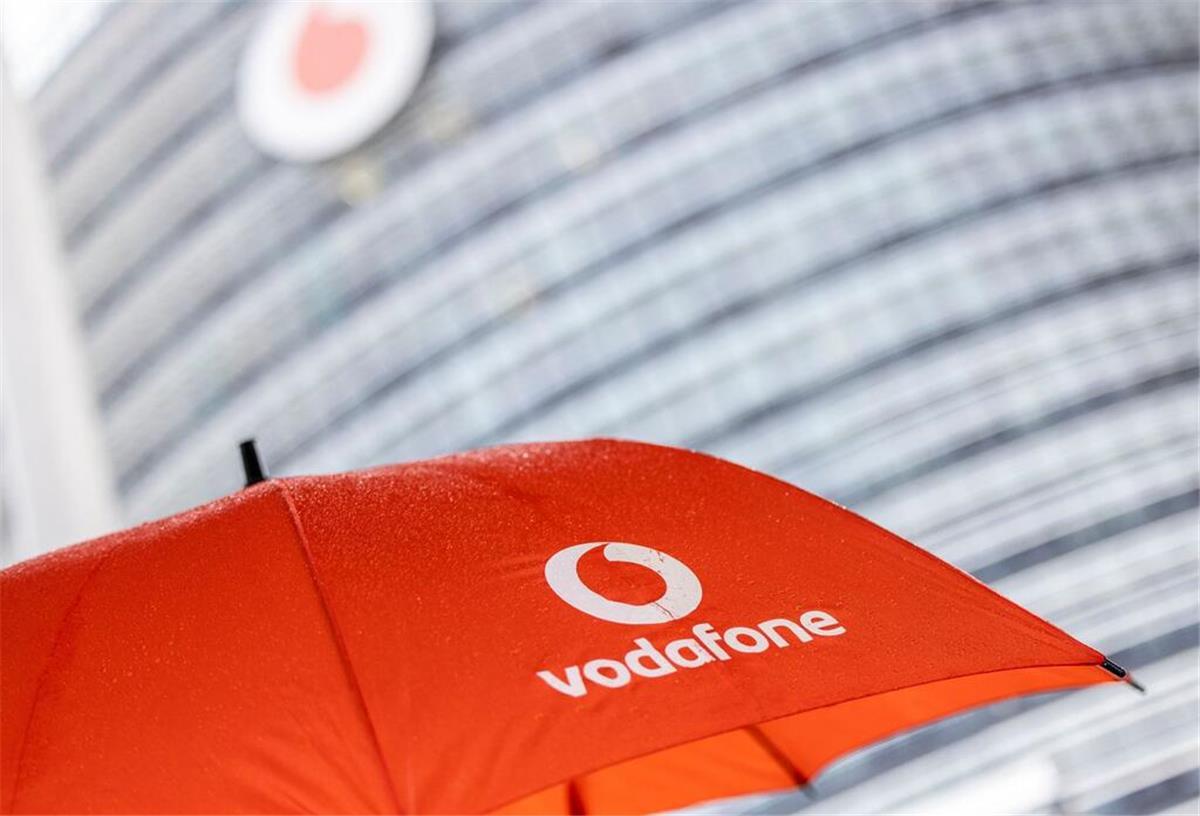 Ein Passant geht mit einem aufgespanntem Regenschirm mit dem Logo von Vodafone an der Konzernzentrale vorbei.