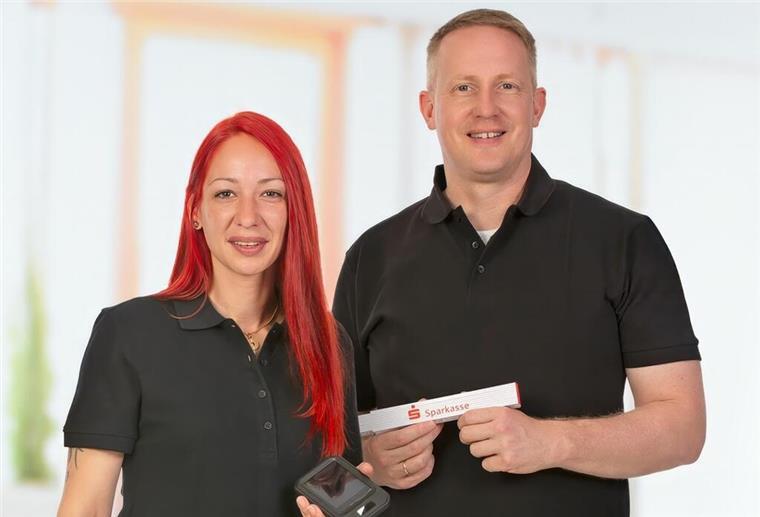 Energie-Experten: Profis von der Weser-Elbe Sparkasse Zwei Energieberater - eine rothaarige Frau und ein blonder Mann in schwarzen Shirts - lächeln in die Kamera und halten ein Sparkasse-Schild in der Hand.