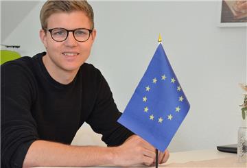 Joshua Henning sitzt in seiner Küche in Breddorf. Die Fahne auf dem Tisch ist ein Geschenk seiner Mutter und steht normalerweise an seinem Bett.