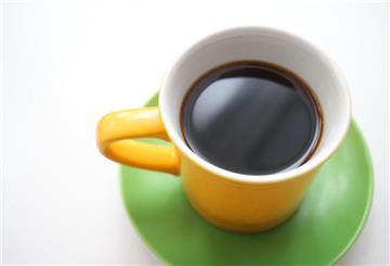 Eine gelbe Tasse mit schwarzem Kaffee steht auf einem Tisch.