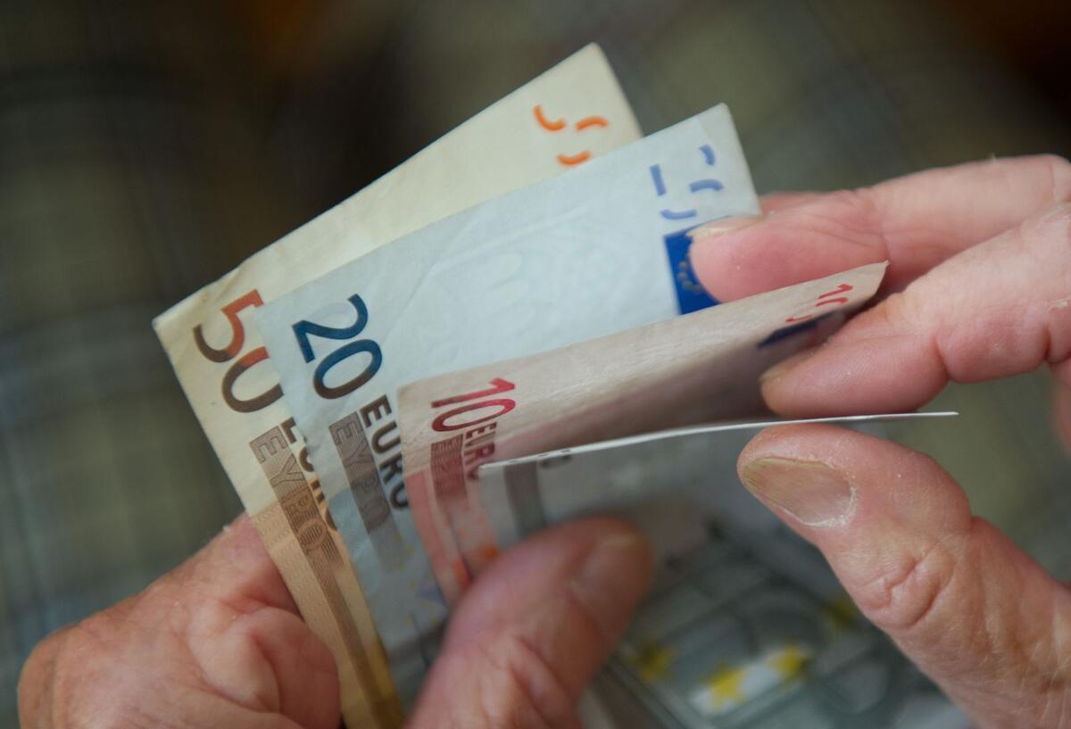 Zwei Hände halten ein paar Geldscheine und zählen sie.