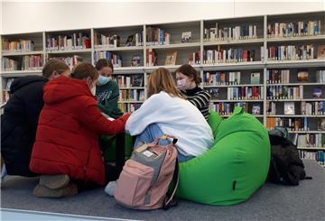 Kinder sitzen in einer Gruppe vor einem Bücherregal.