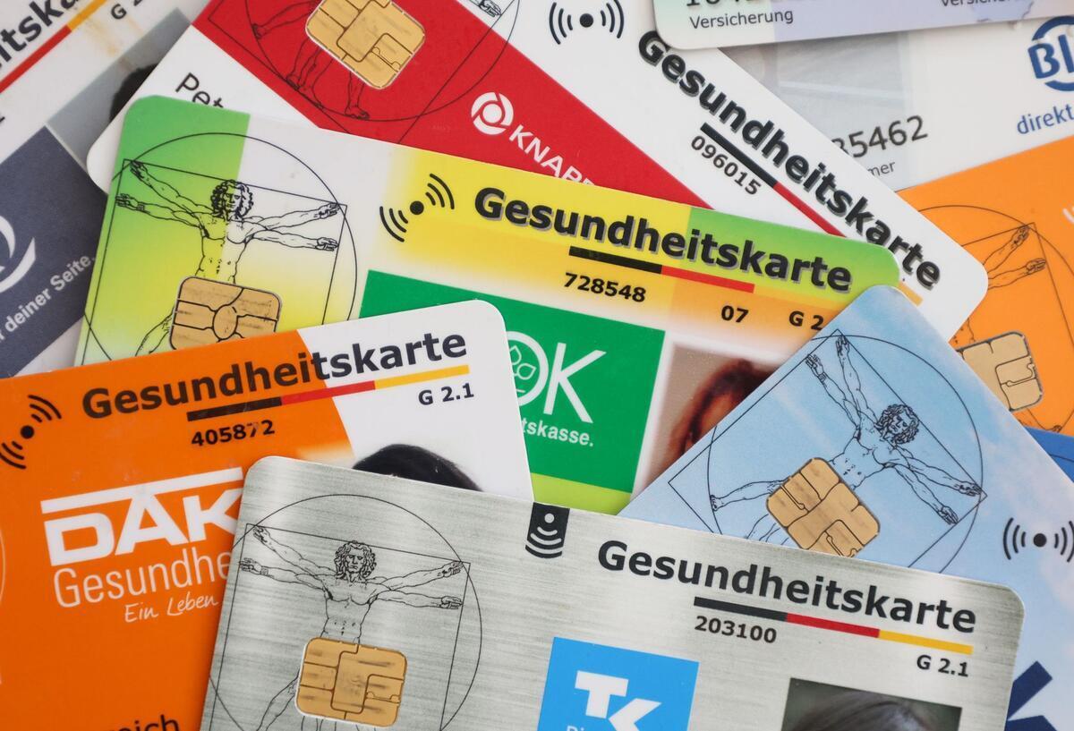 Reform der GKV: Ehepartner sollen 2600 Euro mehr zahlen Symbolbild für Reform der GKV: Eine Auswahl an Gesundheitskarten gesetzlicher Krankenkassen liegen auf einem Tisch.