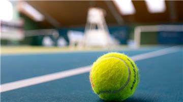 Ein gelber Tennisball liegt auf blauem Teppichboden in einer Tennishalle.