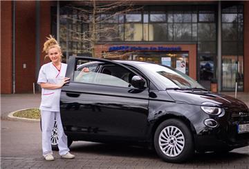 Krankenpflegekraft Marina Popov mit Elektroauto Fiat 500 vor dem Ameos Klinikum Am Bürgerpark.