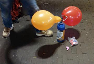 13.11.2024, Hamburg: ILLUSTRATION - Ein Mitarbeiter hält eine Tüte mit Luftballons neben drei Dosen Lachgas und einem Mundstück (weiß) am Tresen eines Kiosks. Der Umgang mit Lachgas als Partydroge besonders bei jungen Leuten könnte in Deutschland bald verboten werden. Das Bundeskabinett billigte dazu einen Entwurf von Gesundheitsminister Lauterbach (SPD), der auch ein Abgabeverbot über Automaten und Spätkaufläden vorsieht. Foto: Marcus Brandt/dpa +++ dpa-Bildfunk +++