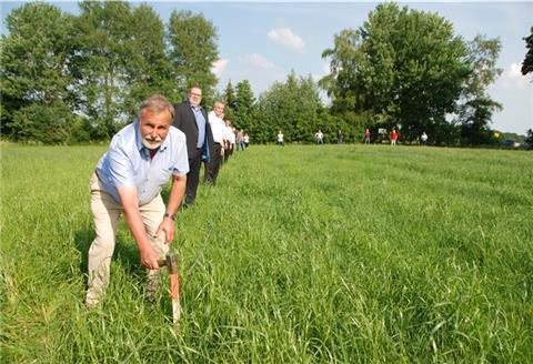 Lintigs Ortsbürgermeister Wilhelm Boldt schlägt den ersten Pflock ein fürs neue Feuerwehrhaus in Lintig. Auch Bürgermeister Thorsten Krüger (dahinter), und Mitarbeiter aus Verwaltung und Fachausschuss und Kameraden der Feuerwehr haben sich aufgestellt, um die Ausmaße des Gebäudes zu verdeutlichen.