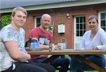 Madlen und Thomas Kühl sitzen mit Sohn Louis im Garten vor dem Haus der Familie.