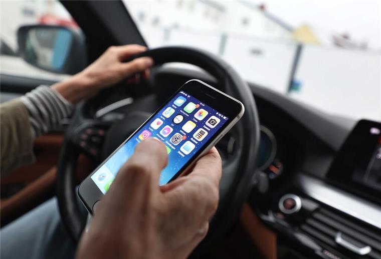 Handy am Steuer: Was erlaubt ist – und was richtig teuer wird Ein Mann blickt auf sein Handy während er ein Auto fährt.