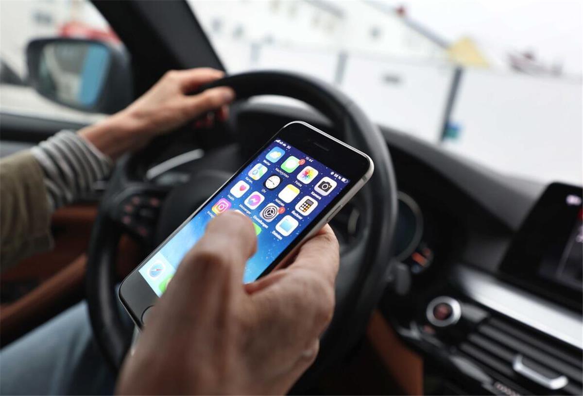 Ein Mann blickt auf sein Handy während er ein Auto fährt. 