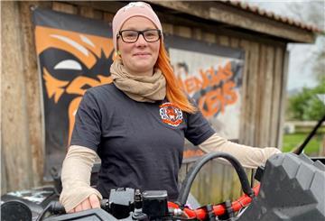 Eine junge Frau sitzt auf ihrem Quad. Sie hat rote Haare und trägt ein schwarzes T-Shirt und eine rosa Mütze. 