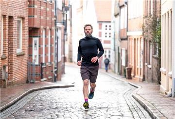 Ein Mann joggt über eine Kopfsteinpflasterstraße. Daneben sind alte Häuser zu sehen.