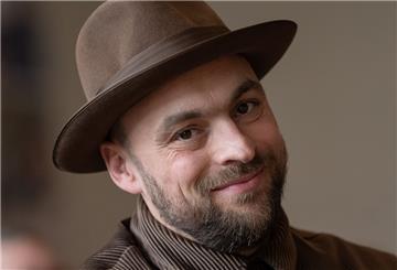 Max Mutzke trägt einen Hut und lächelt.