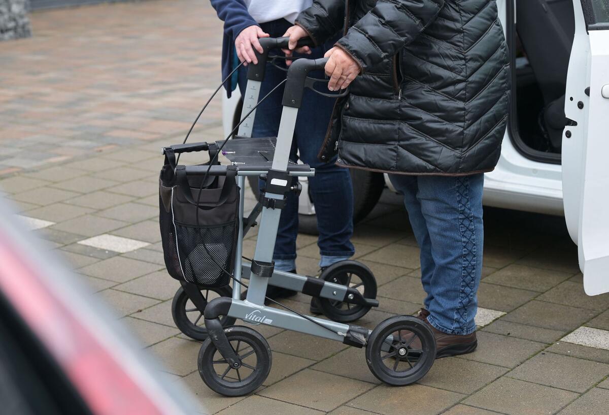 Eine pflegebedürftige Seniorin beim Aussteigen aus einem Auto.