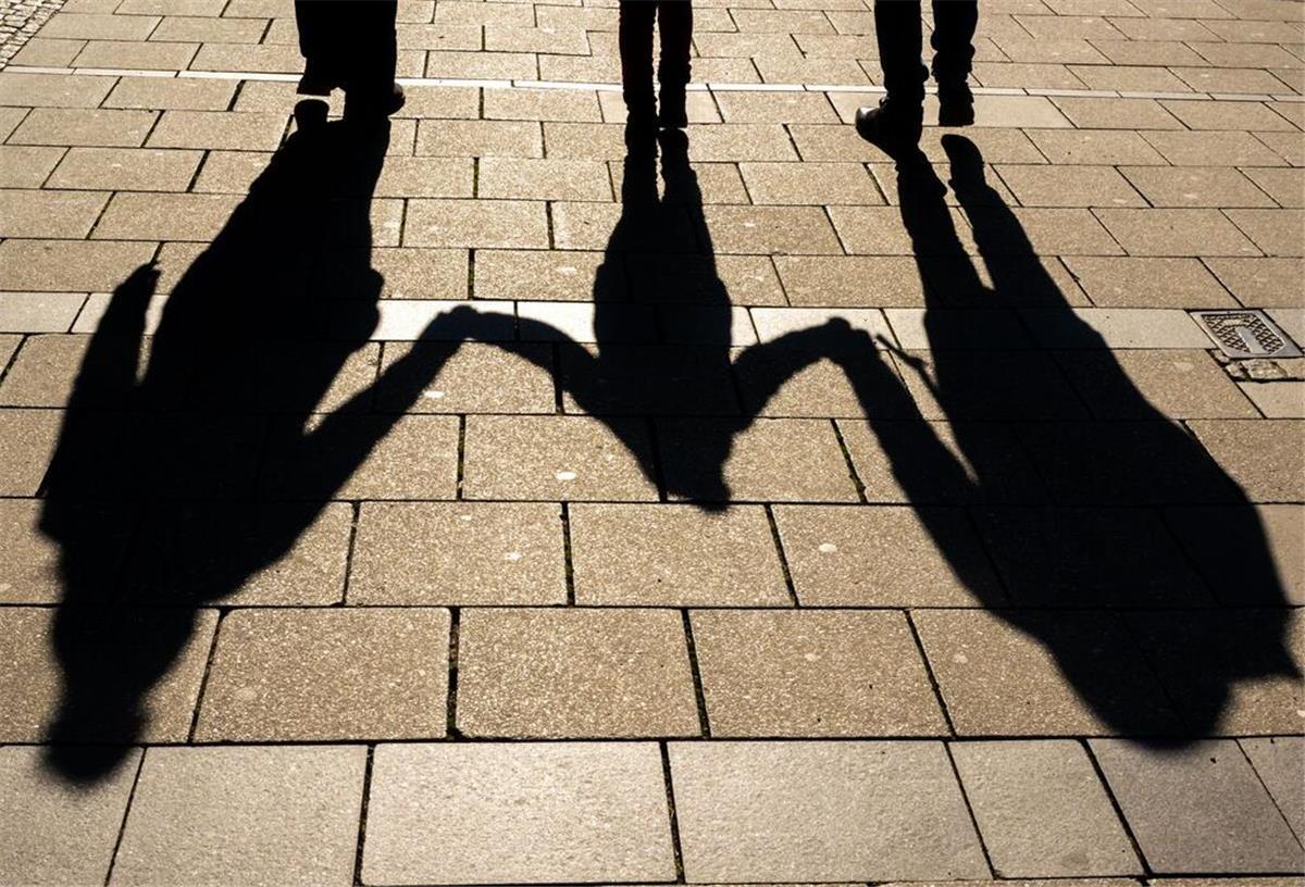 Die Schatten von zwei Erwachsenen und einem Kind fallen in den Morgenstunden auf den Asphalt. Das Kindergeld wird erhöht.