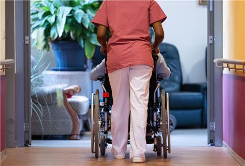 Eine Bewohnerin eines Pflegeheims wird von einer Pflegerin einen Gang entlang geschoben.