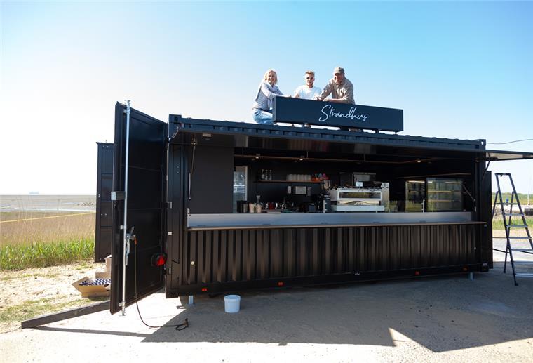 Michaela, Leonard und John Reinhardt testen den Sitz der gerade installierten „Strandhus“-Aufschrift auf dem Dach des Cafébar-Containers am Strand von Wremen.