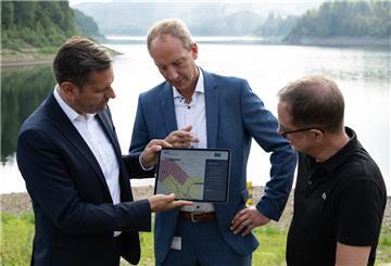 Olaf Lies, Christoph Donner und Maik Uhlen stehen mit einem Tablet an der Sösetalsperre im Harz.