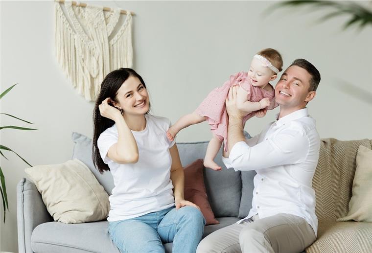 Familienzeit im Traumhaus? Mit dieser Checkliste klappt es sicher! Paar sitzt mit Baby auf dem Sofa