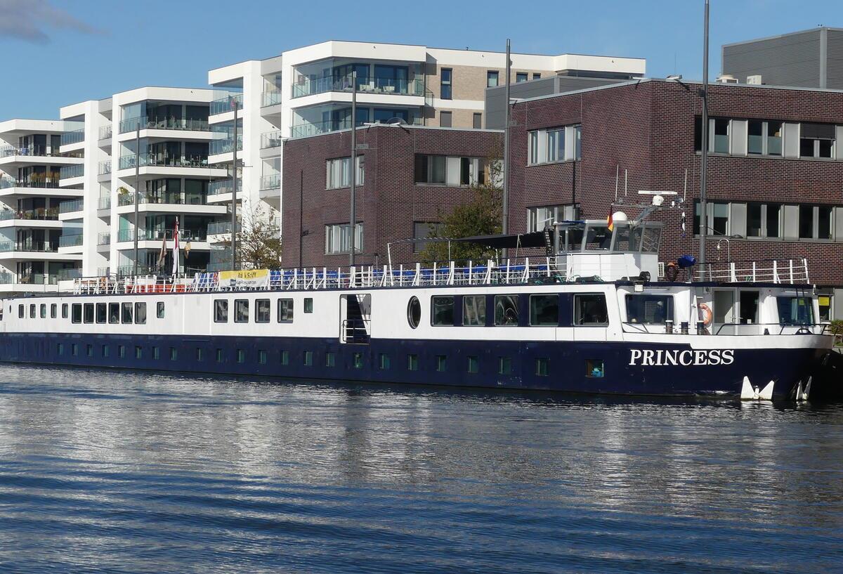 Das Flusskreuzfahrtschiff „Princess“ liegt am Kai in Bremerhaven. Im Hintergrund moderne Wohn- und Bürogebäude, das Schiff spiegelt sich im Wasser.