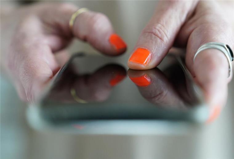 Unbekannter Anruf? So findest du kostenlos den Namen zur Nummer Eine Frau mit orangefarbenem Nagellack hält ein Handy in der Hand.