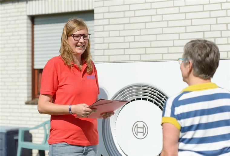 Eine junge Frau berät eine ältere Dame zum Thema Wärmepumpen. Im Hintergrund ist eine Wärmepumpe zu sehen.