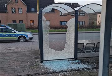 Die Scheibe eines Wartehäuschens in Dorum ist zersplittert. Scherben liegen auf dem Boden. Dahinter fährt ein Polizeiauto.