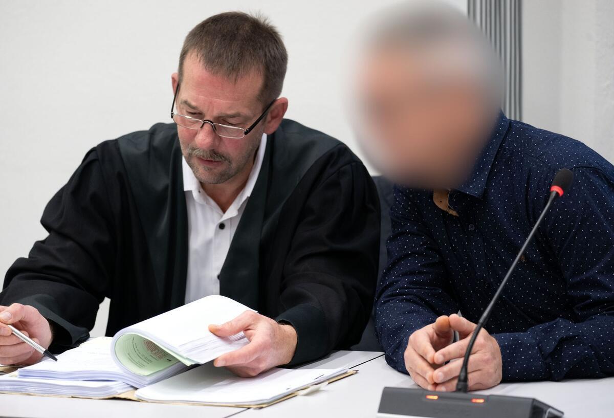 Mit gefalteten Händen sitzt der Angeklagte (r) neben seinem Verteidiger und wartet auf den Beginn der Verhandlung. In Bamberg hat der Prozess gegen einen Mann begonnen, der mehrfach versucht haben soll, seine Partnerin mit Pflanzengiften zu töten, um mit einer Online-Bekanntschaft ein neues Leben zu beginnen.
