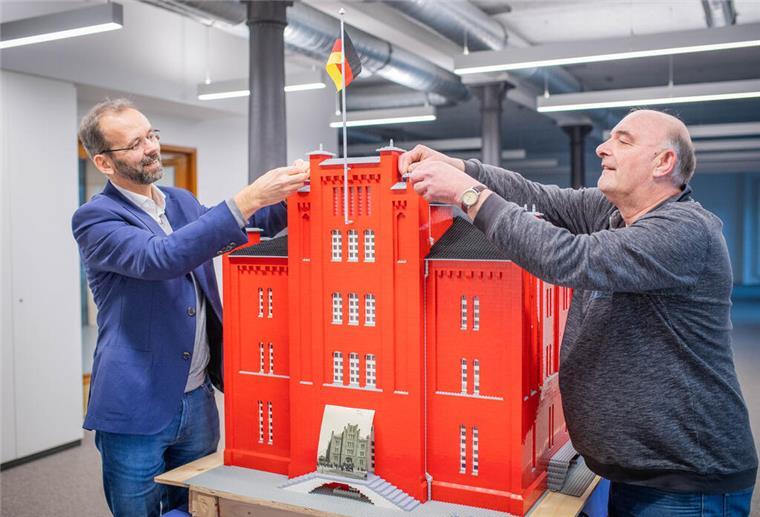 Maurer baut alten Backstein-Speicher aus Legosteinen nach Zwei Männer arbeiten an einem großen roten Gebäude aus Legosteinen.