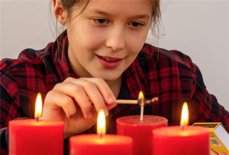 Sicher durch die Weihnachtszeit Vorsicht vor Verbrennungen: Mädchen zündet Adventskerzen an.