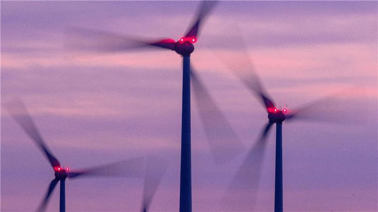 Wirtschaft fordert noch mehr Tempo bei Energiewende Mit Signallampen beleuchtete Windräder drehen sich nach Sonnenuntergang.