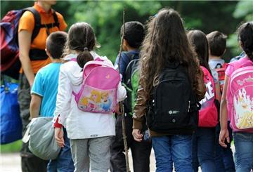 Schulkinder laufen mit ihrer Lehrerin durch einen Wald. 