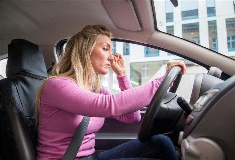 Frau sitzt müde am Steuer eines Autos