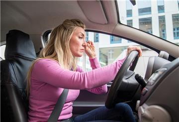 Frau sitzt müde am Steuer eines Autos
