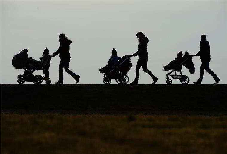Mütterrente: Einfacher Antrag bringt dir 118 Euro mehr Geld jeden Monat pro Kind In einem Schattenrist ist zu sehen, wie drei Erwachsene jeweils einen Kinderwagen schieben, in dem Kinder sitzen.