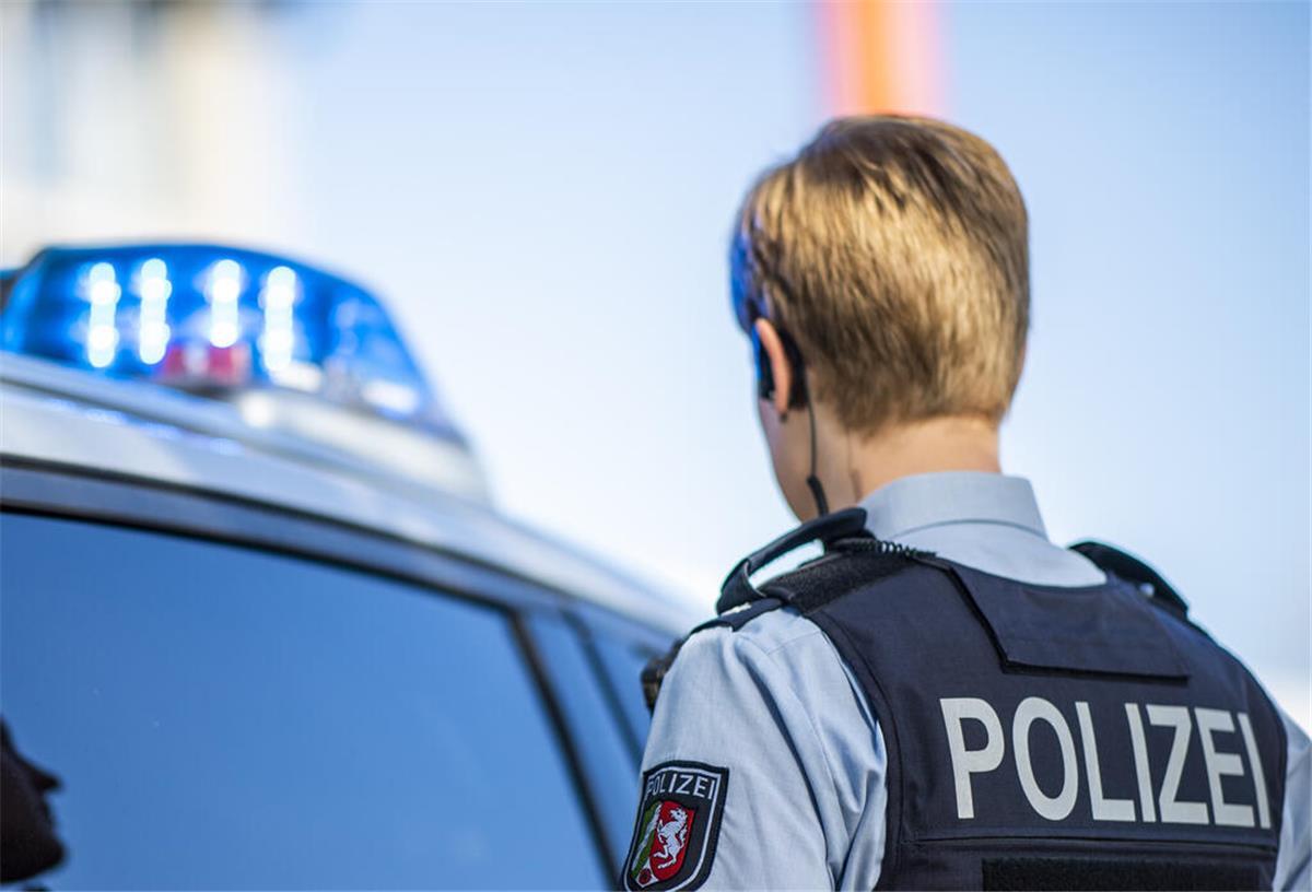 Eine Polizistin steht vor einem Streifenwagen, dessen Blaulicht leuchtet